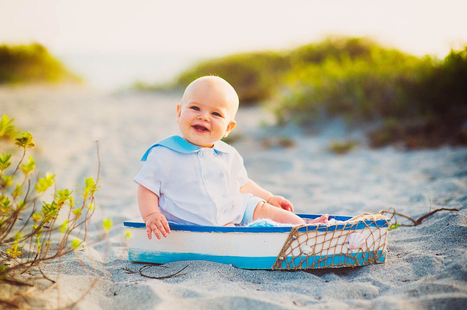 Smiling baby boy sitting in a small wooden boat on the Sarasota beach
