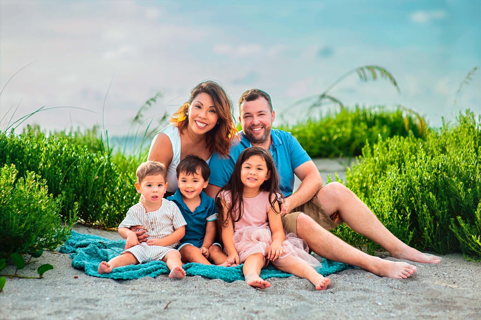 Family of five sitting together on the sand in Sarasota with lush greenery in the background