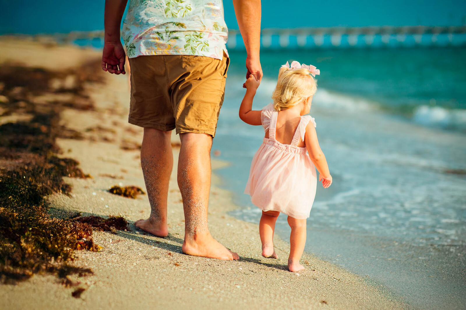 Father and daughter holding hands, walking barefoot along the Sarasota shoreline