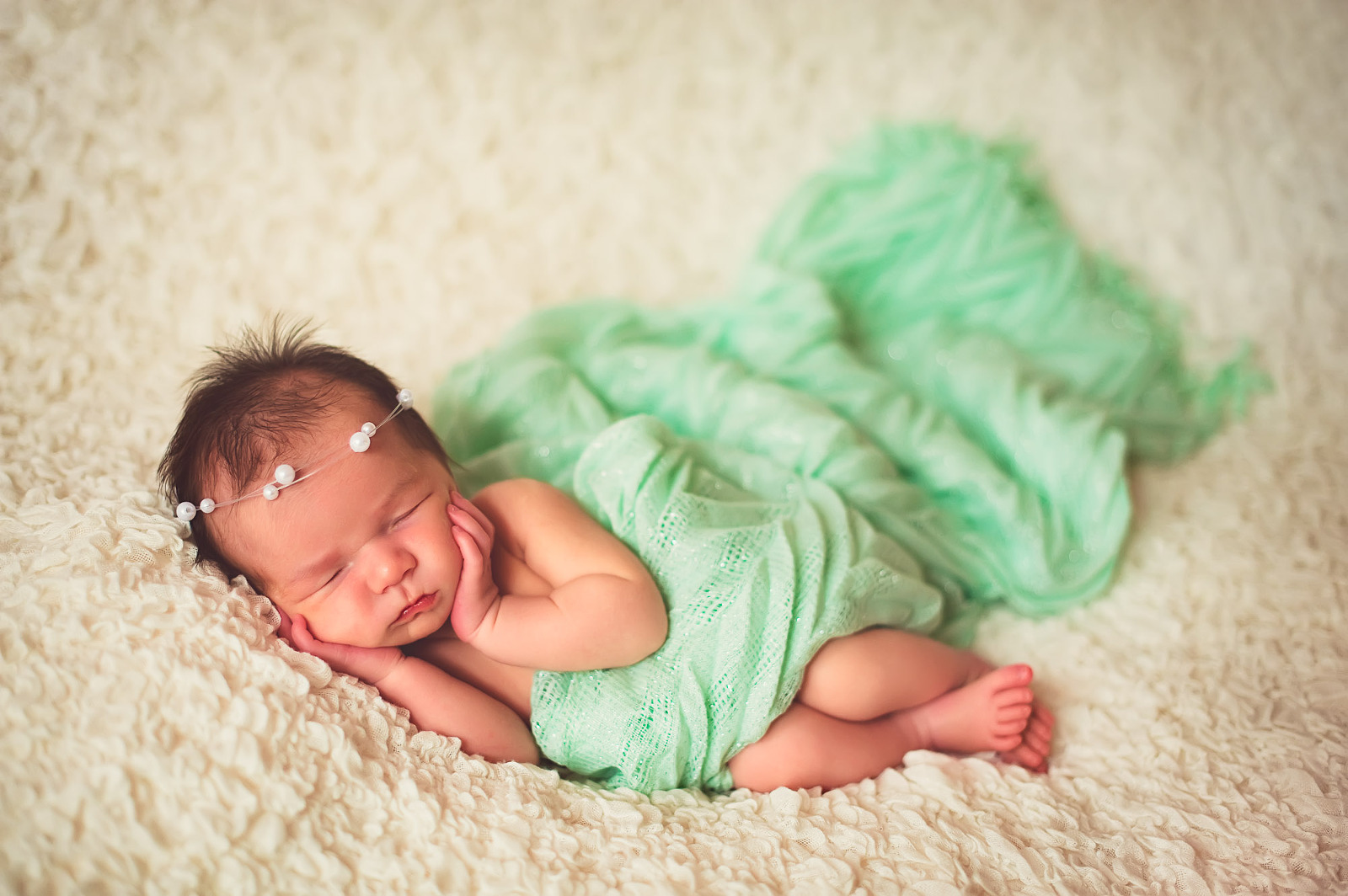 Newborn baby girl in a soft mint wrap with flowing fabric and delicate pearl headband, photographed in Sarasota