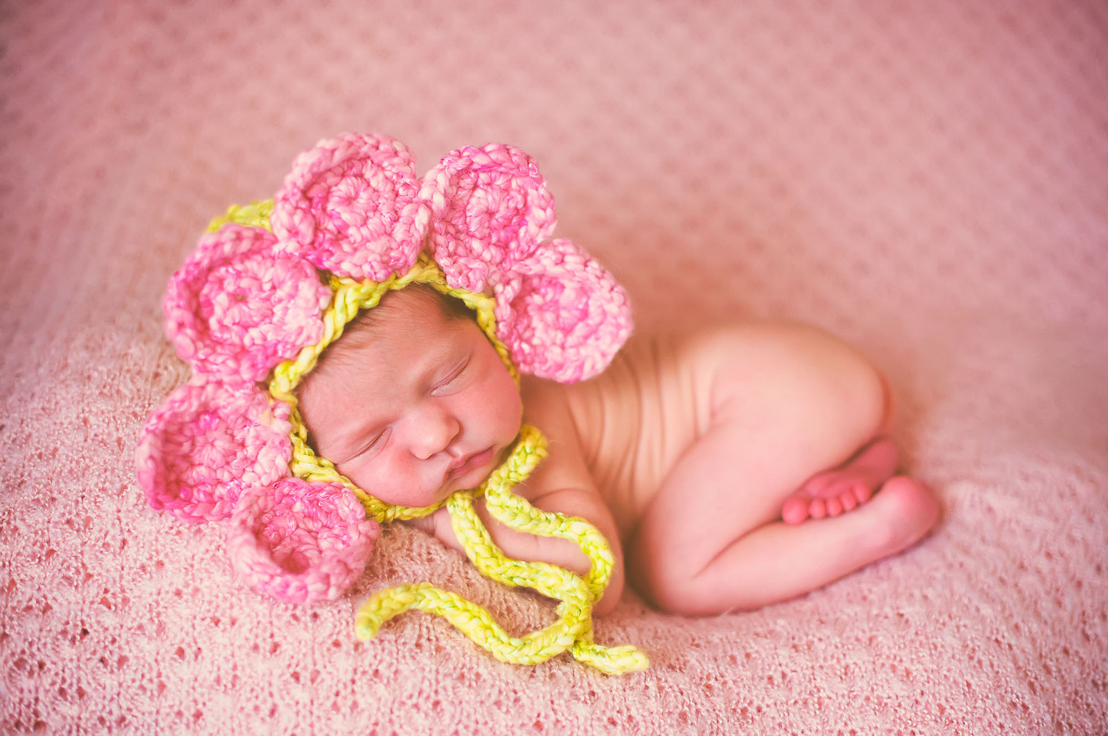Newborn baby girl peacefully sleeping in a pink crochet flower bonnet on a textured pink blanket in Sarasota