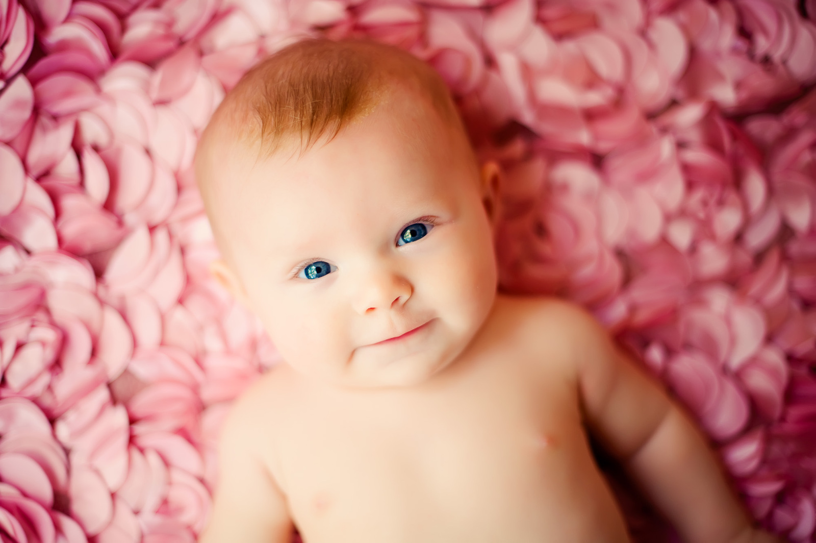 Baby girl smiling while laying on a bed of soft pink floral rosettes