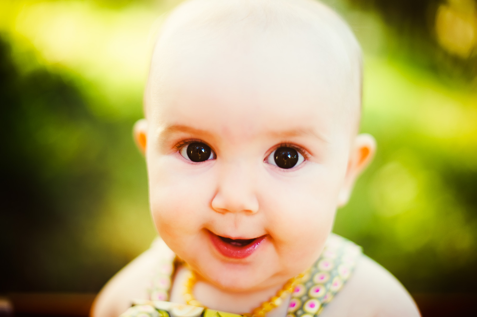 Close-up portrait of a smiling baby with wide, expressive eyes taken outdoors in Sarasota