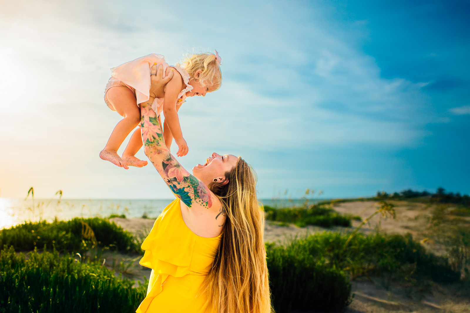 Mother lifting daughter into the air at Sarasota beach with sunset glow