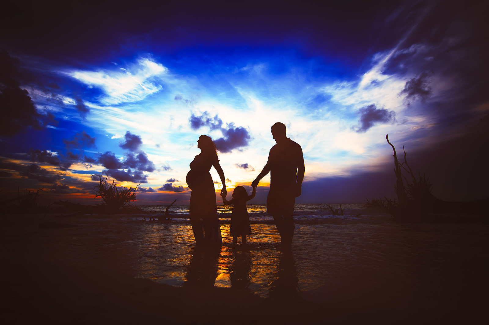 Silhouette of pregnant mother, father, and child during a Sarasota beach sunset maternity session