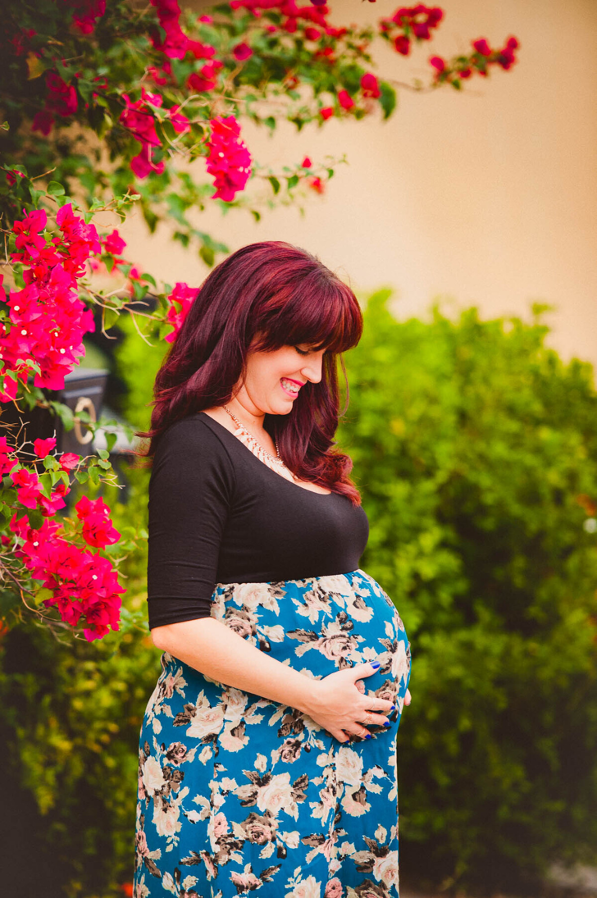 Pregnant woman in a floral dress standing next to bright pink bougainvillea in Sarasota