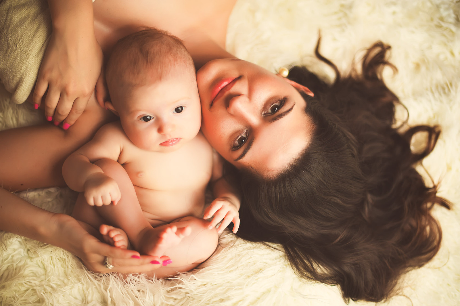 Mother and baby lying together on a soft surface, gazing with serene expressions during a baby photo session in Sarasota