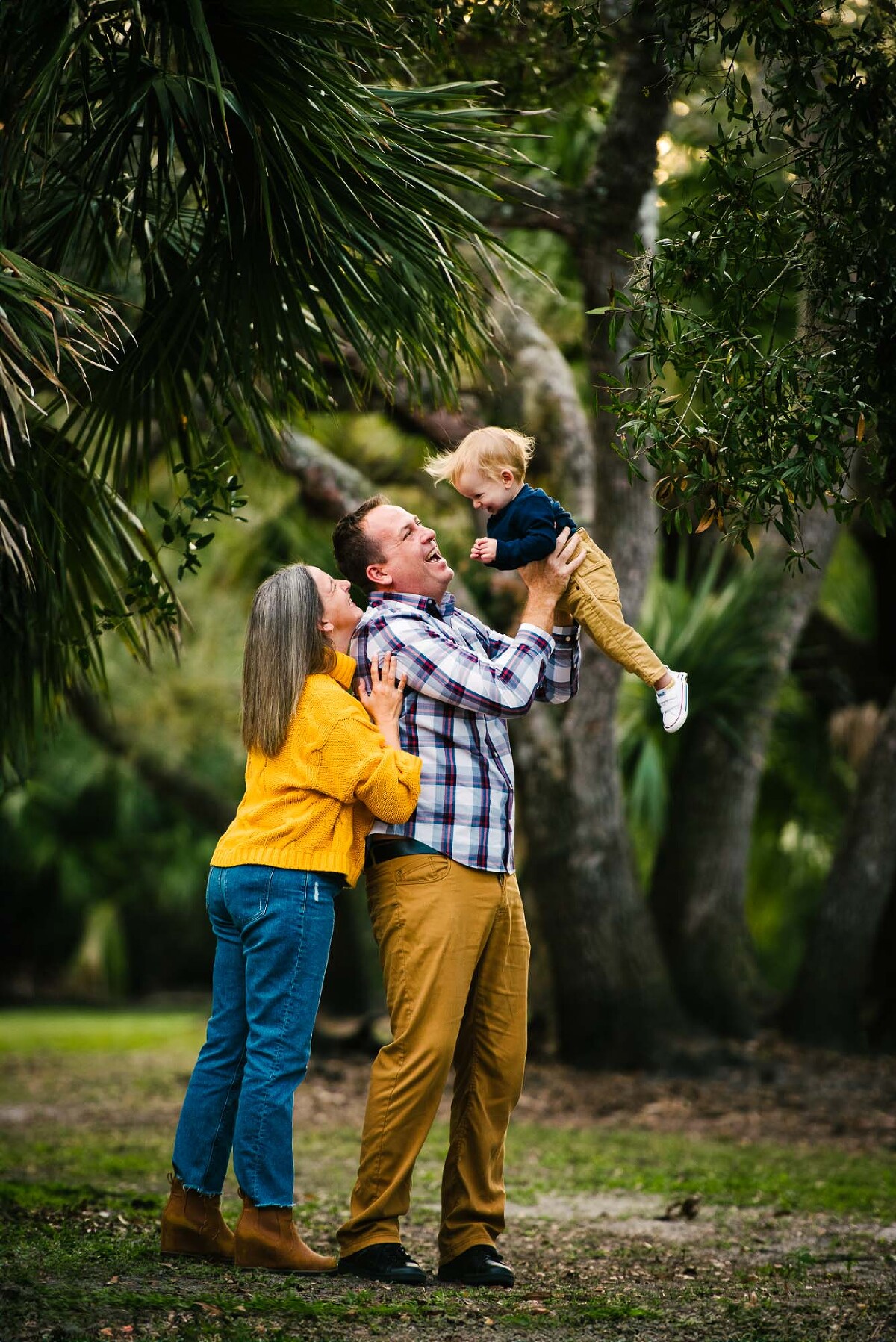 Family playing in wooded Sarasota park with toddler lifted in the air