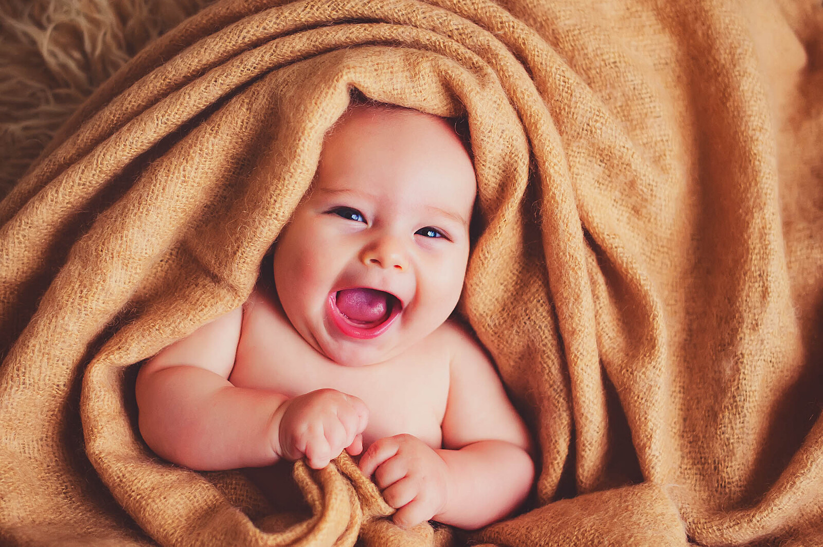 Happy baby smiling while wrapped in a warm tan blanket during a newborn session in Sarasota